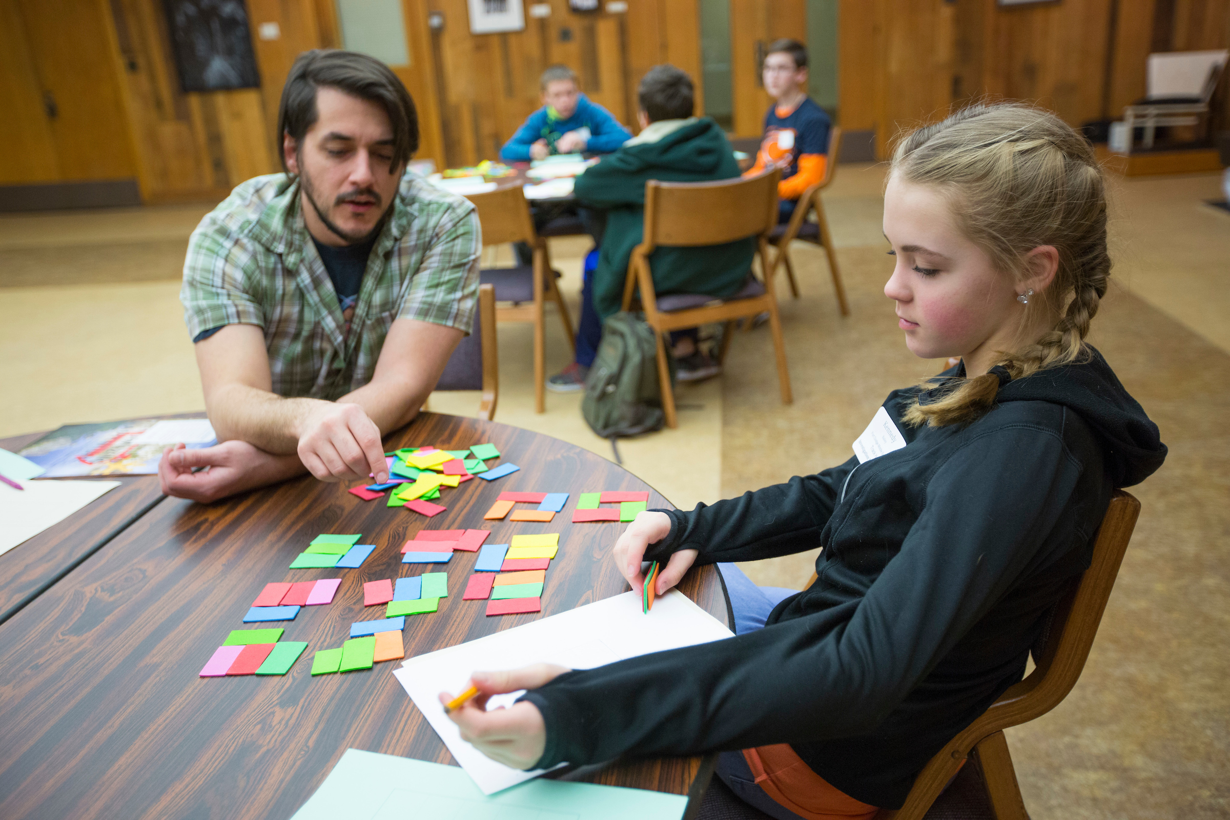 Kris Lee of the math department leads students in a tiling and pattern exercise using colorful foam tiles at a table in the Memorial Union.